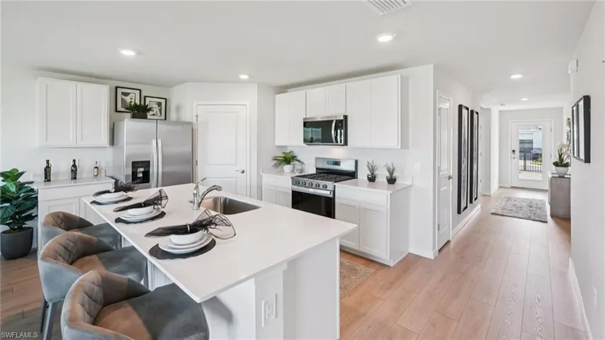 Modern kitchen featuring a large island with sink, stainless steel appliances, white cabinetry, and wood-finish flooring