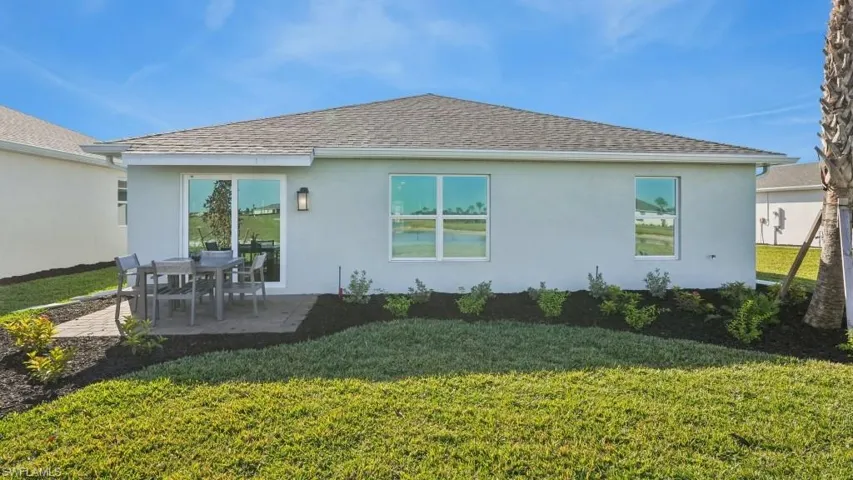 Rear exterior featuring a paver patio with a sliding glass door entry, multiple windows, and a landscaped perimeter