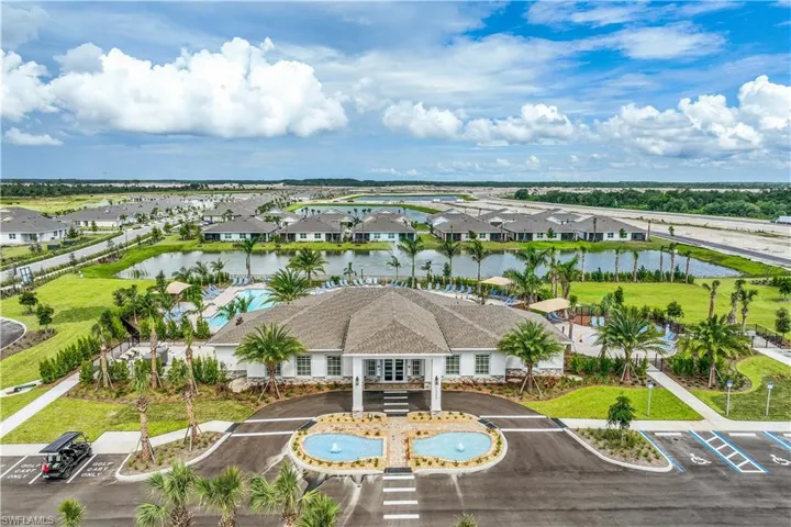 Community clubhouse featuring a paver driveway, dual fountain entrance, resort-style swimming pool, and surrounding green spaces
