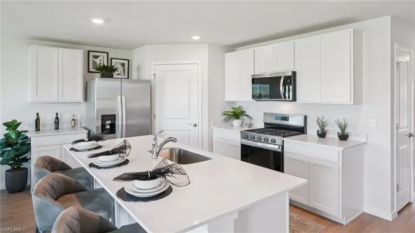 Kitchen featuring a white countertop island with integrated sink, white cabinetry, and stainless steel appliances including a refrigerator, range, and microwave