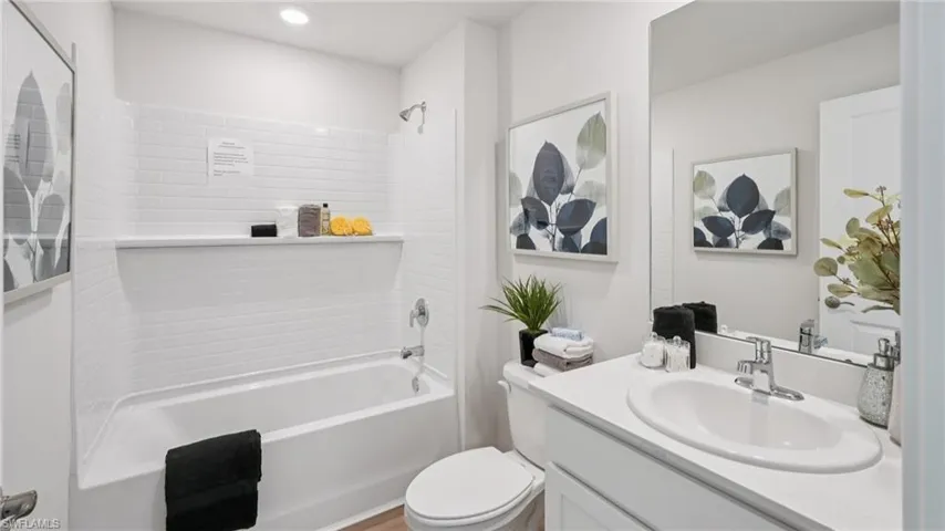 Bathroom featuring a white subway tile shower surround with an integrated ledge, a white bathtub, and a vanity with a white countertop and undermount sink