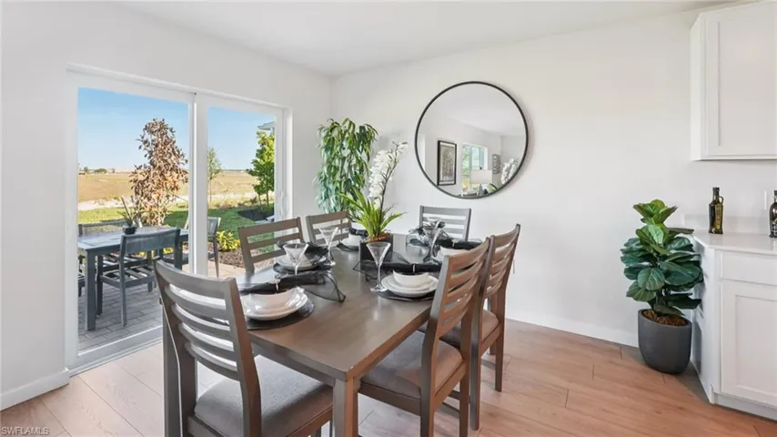 Bright dining area featuring wood-finish flooring, a contemporary dark wood table with seating for six, and white shaker-style cabinetry with a light-colored countertop
