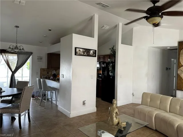 Living area with dark tile patterned floors, a ceiling fan, baseboards, high vaulted ceiling, and a chandelier
