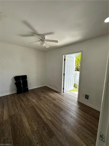 Unfurnished living room featuring dark wood-type flooring, ceiling fan, and baseboards