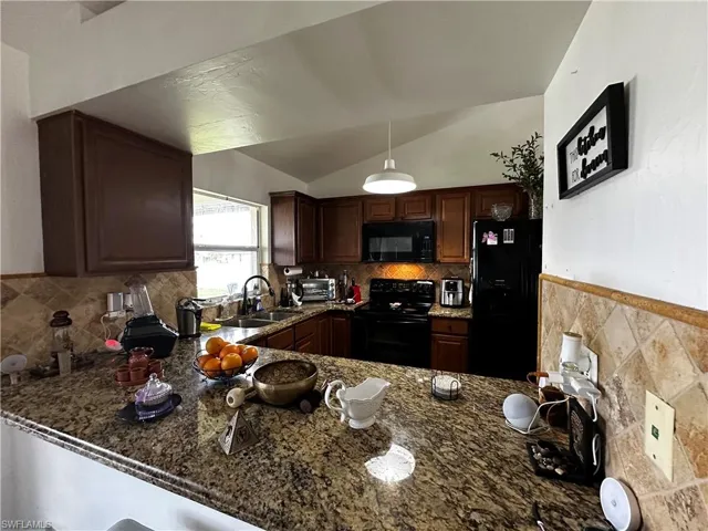 Kitchen featuring black appliances, a sink, a peninsula, dark stone counters, and vaulted ceiling