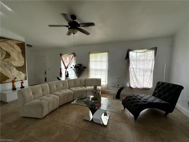 Living room with a ceiling fan, tile patterned floors, and baseboards