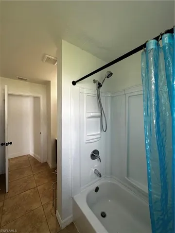 Bathroom featuring shower / bathtub combination with curtain, tile patterned floors, and baseboards