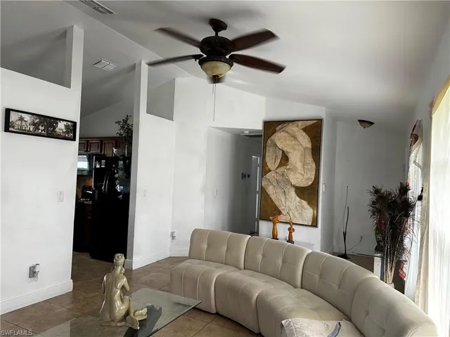 Tiled living room featuring a ceiling fan, lofted ceiling, and baseboards