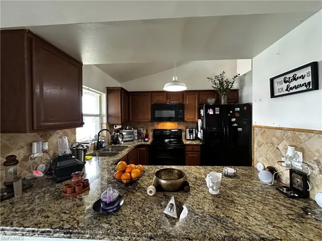 Kitchen featuring black appliances, a sink, lofted ceiling, a peninsula, and dark stone countertops