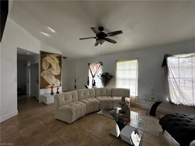 Living room with ceiling fan, tile patterned flooring, baseboards, and lofted ceiling
