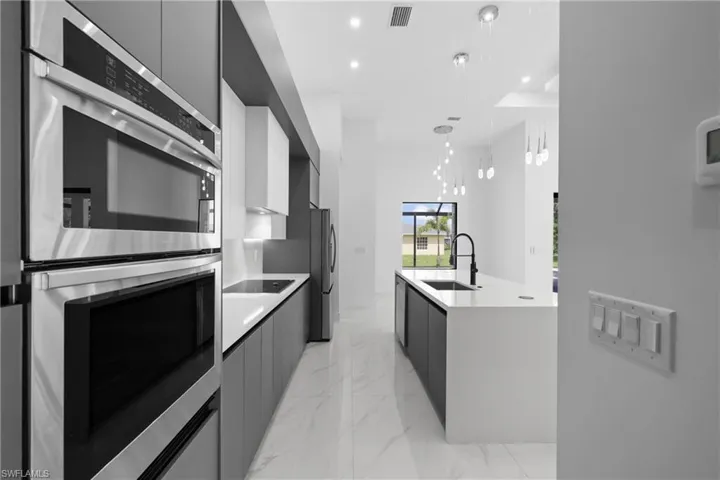 Kitchen featuring modern cabinets, appliances with stainless steel finishes, light countertops, light marble finish flooring, and recessed lighting