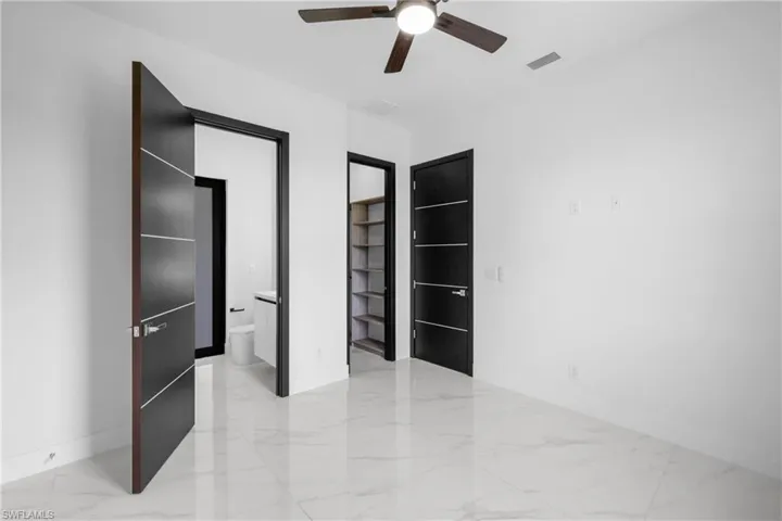 Unfurnished bedroom featuring light marble finish flooring, ensuite bathroom, and a ceiling fan
