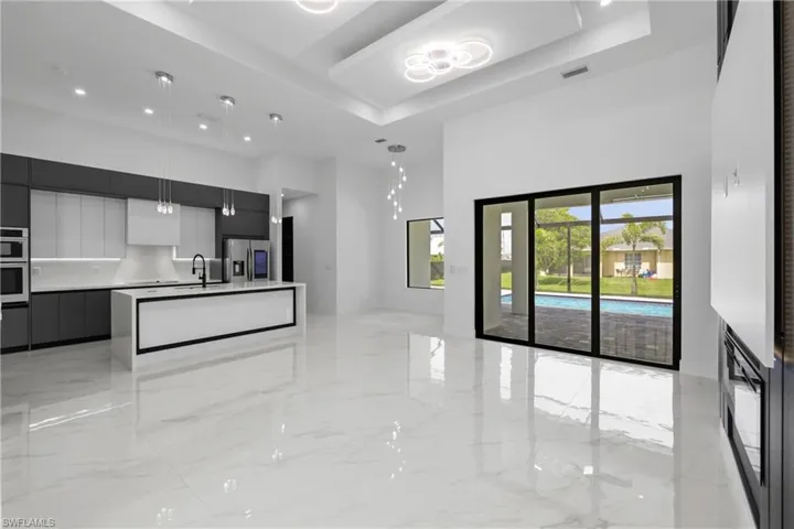 Kitchen featuring modern cabinets, stainless steel fridge with ice dispenser, a towering ceiling, light marble finish flooring, and open floor plan