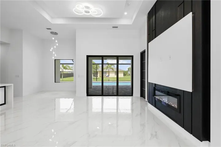 Unfurnished living room with light marble finish flooring, a towering ceiling, a glass covered fireplace, and a raised ceiling