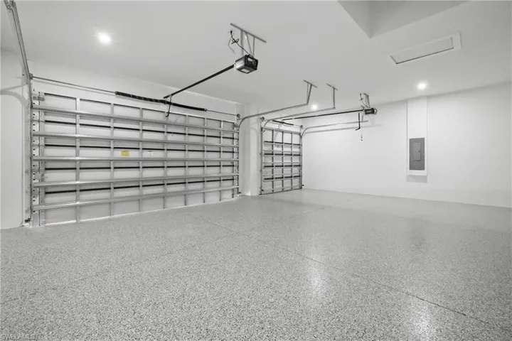 Garage with a garage door opener, electric panel, and recessed lighting
