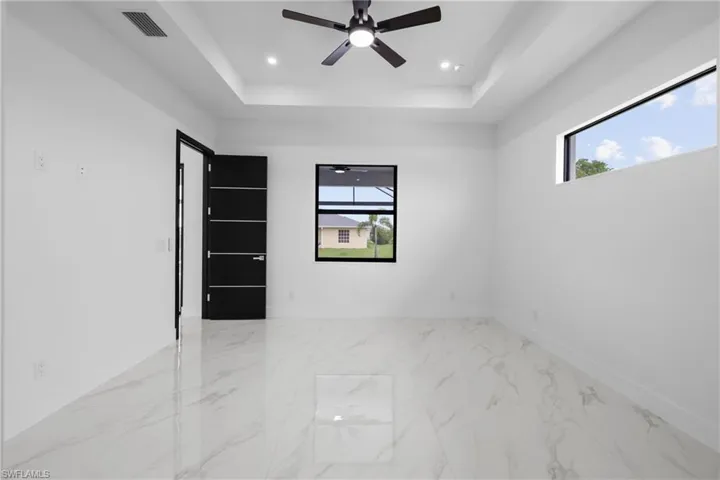 Unfurnished room featuring a tray ceiling, healthy amount of natural light, light marble finish flooring, ceiling fan, and recessed lighting