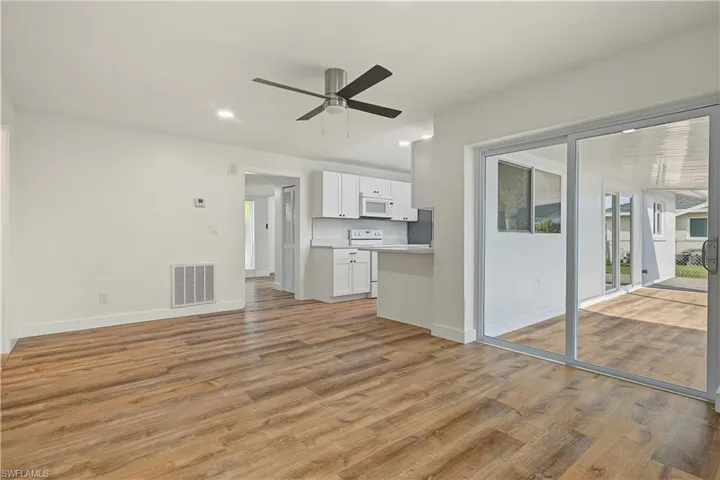 Open-concept interior featuring wood-finish flooring, white cabinetry, recessed lighting, a ceiling fan, and sliding glass doors leading to an enclosed porch