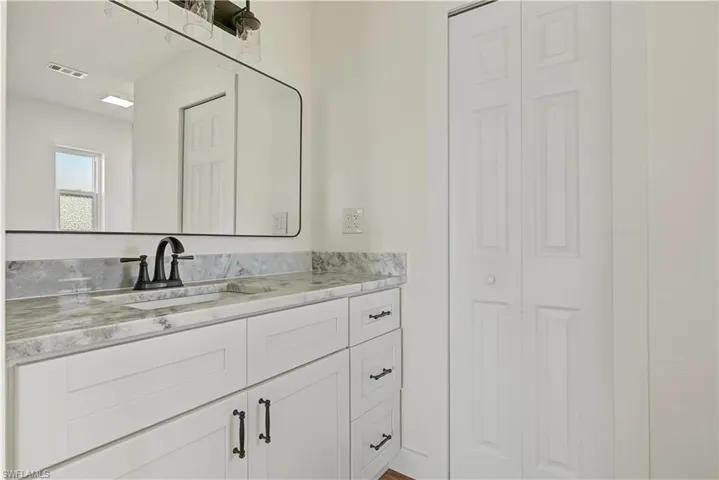 White vanity with a stone countertop, under-mount rectangular sink, matte black hardware, and an expansive wall-mounted mirror