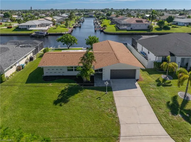 Waterfront property featuring a canal-side location, concrete driveway, attached garage, and landscaped lawn with mature trees