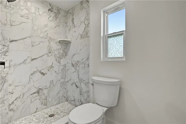 Walk-in shower featuring large-format patterned wall tile, integrated corner shelving, and textured stone-finish flooring