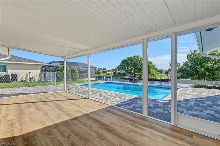 Screened-in lanai featuring wood-finish flooring, paver patio, and an inground swimming pool overlooking a canal