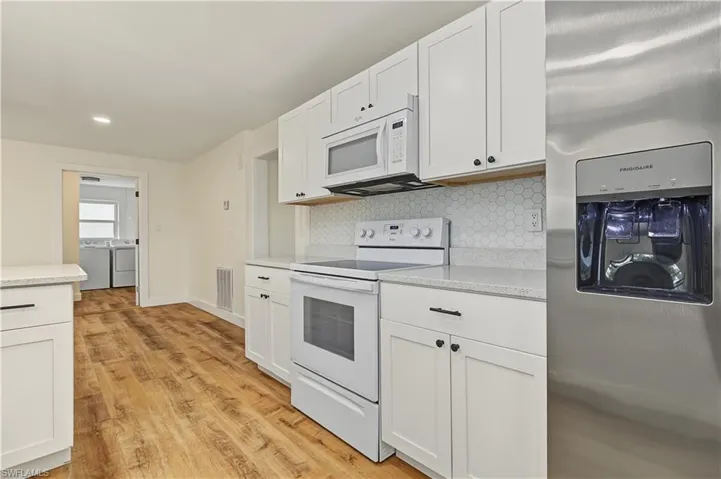 Kitchen featuring white cabinetry with matte black hardware, stone-finish countertops, a white hexagonal tile backsplash, stainless steel refrigerator, and wood-finish flooring
