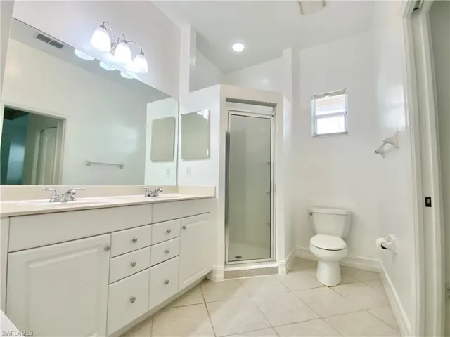 Bathroom featuring an enclosed shower, double vanity, tile patterned flooring, and toilet