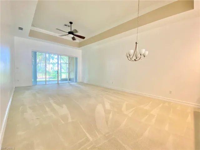 Carpeted empty room with a tray ceiling and ceiling fan with notable chandelier