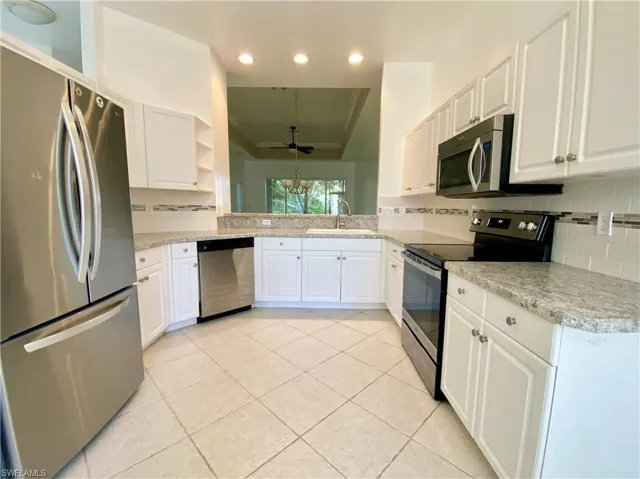 Kitchen featuring decorative backsplash, ceiling fan, white cabinetry, appliances with stainless steel finishes, and sink