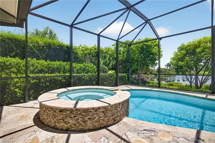 Screened outdoor enclosure featuring a swimming pool, stone-clad spa, and a flagstone patio