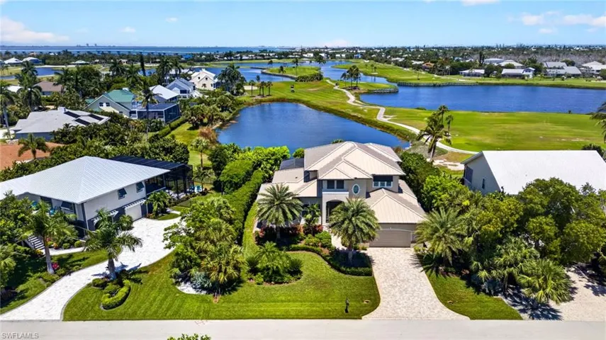 Expansive property featuring a paver driveway, lush green lawns, mature landscaping with palm trees, and a two-story residence with a multi-gabled roofline