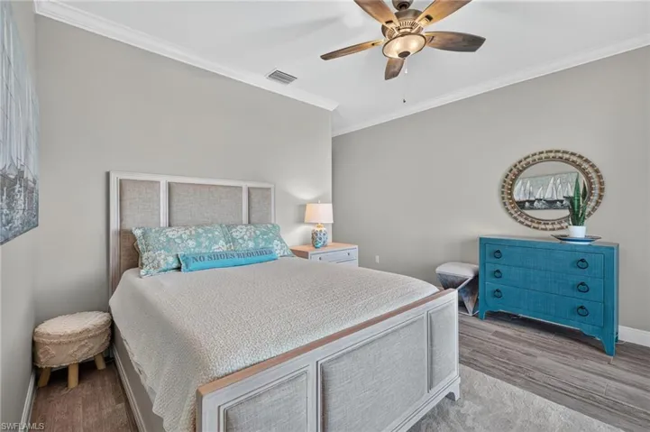 Spacious bedroom featuring wood-finish flooring, a ceiling fan with integrated lighting, crown molding, and a built-in upholstered bed frame