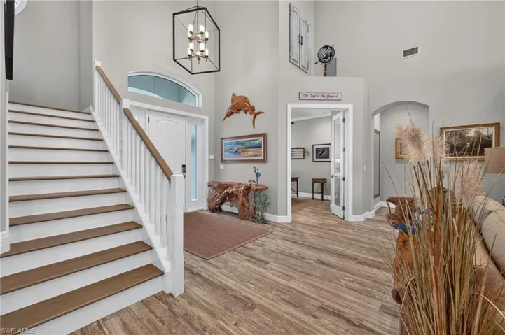 Entryway featuring a two-story ceiling, wood-finish flooring, a white staircase with wood handrail, an arched transom window, and a black geometric chandelier