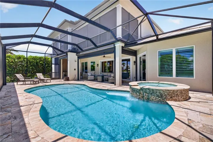 Screened outdoor area featuring a freeform pool with integrated spa and stone surround, surrounded by stone paver decking