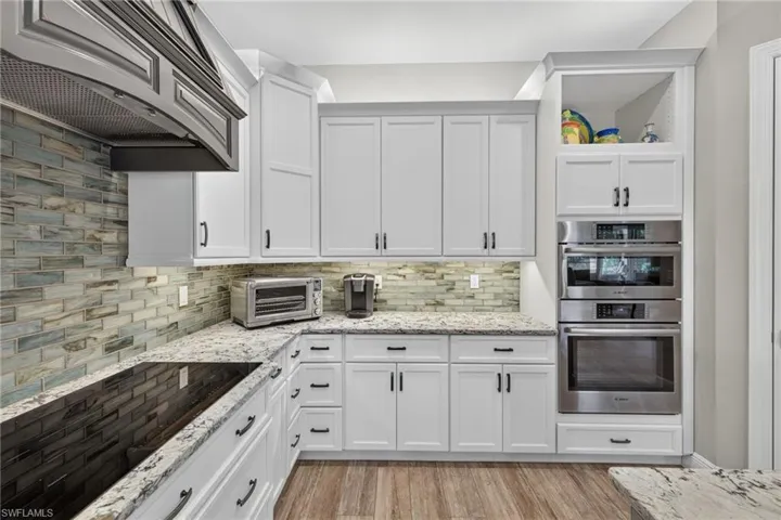 Kitchen featuring white shaker-style cabinetry, light granite countertops, and a full tile backsplash