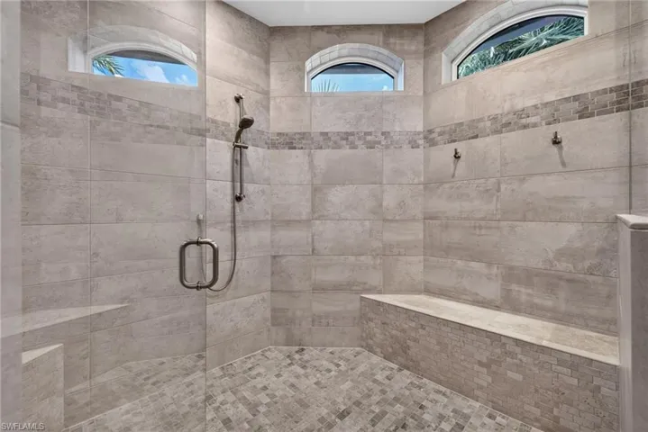 Primary Bathroom w/ Spacious walk-in shower featuring large format wall tiles, a mosaic tile accent band, and coordinating mosaic floor tiles