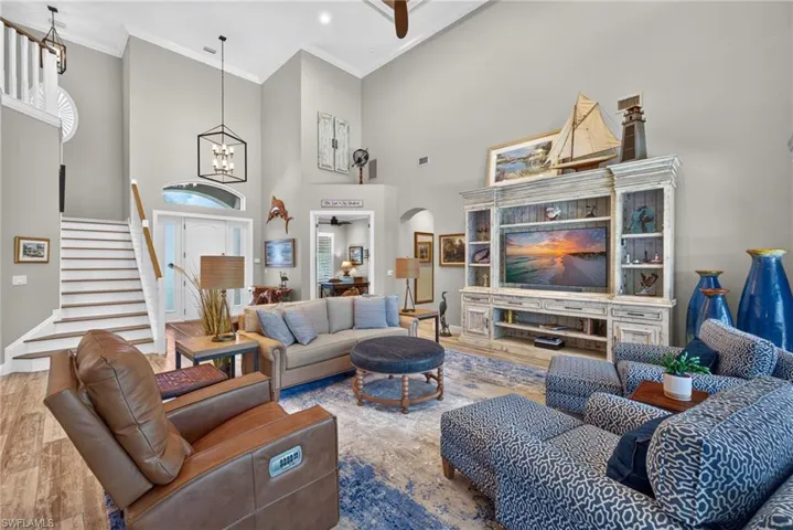 Expansive living area featuring soaring vaulted ceilings, wood-finish flooring, a contemporary chandelier, and a white staircase with wood handrails