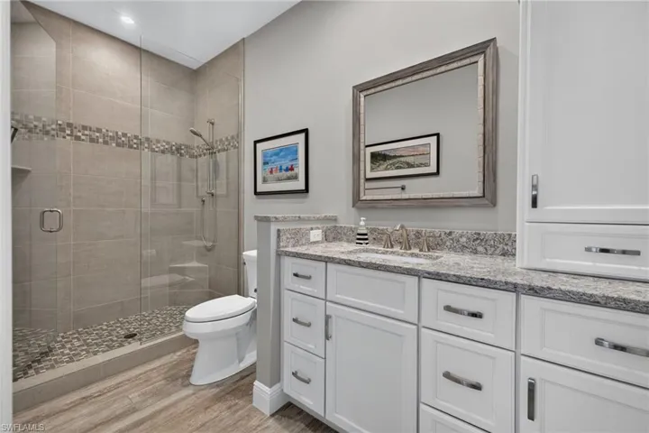Full bathroom featuring a glass-enclosed shower with pebble-style flooring and a mosaic tile accent strip