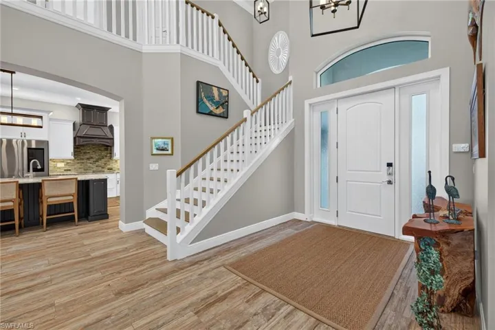 Two-story foyer featuring an arched transom window, a white paneled entry door with frosted glass sidelights, wood-finish flooring, and a staircase with white balusters and wood handrails