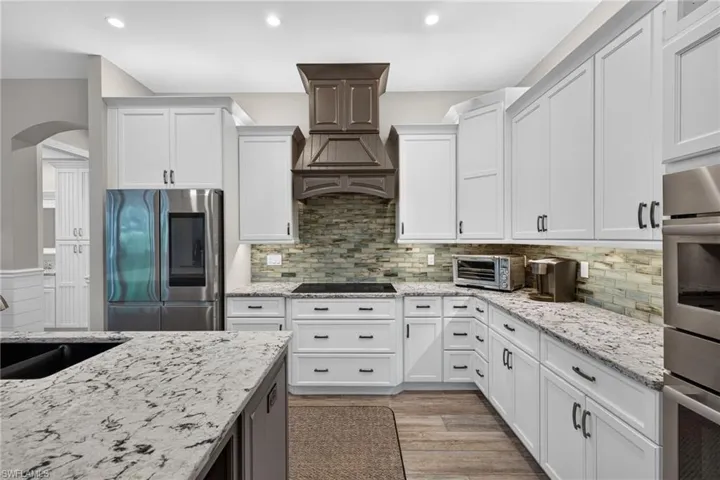 Kitchen featuring white shaker-style cabinetry, light-toned countertops, stone mosaic backsplash, wood-finish flooring, and stainless steel appliances