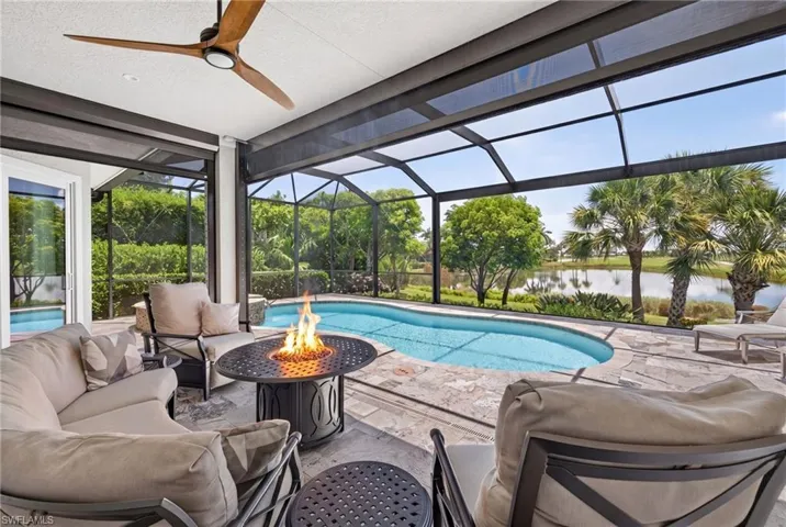 Screened lanai featuring a built-in swimming pool, stone paver patio, wood-finish ceiling fan, and a gas fire pit
