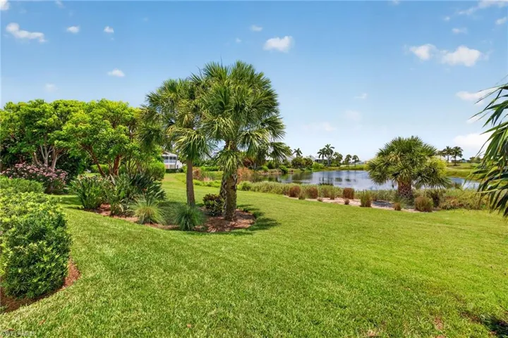 Expansive green lawn with mature palm trees and diverse shrubbery, bordering a serene body of water