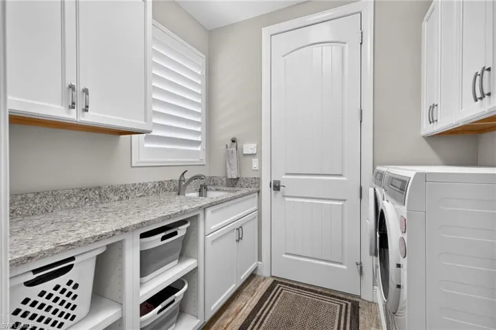 Utility room featuring white shaker cabinetry, an integrated sink, granite-style countertops, and wood-finish flooring