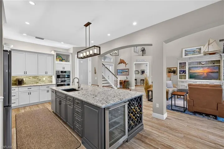 Gourmet kitchen featuring a large central island with light granite countertops, a built-in wine refrigerator, and a deep basin sink