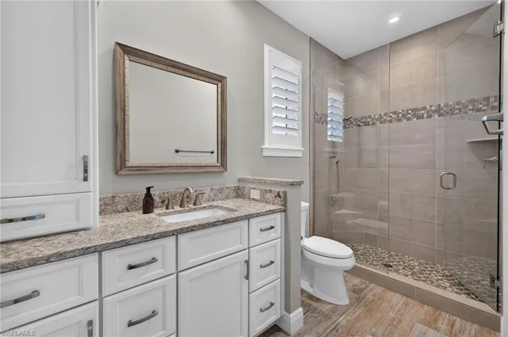 Bathroom featuring a frameless glass shower enclosure, stone pebble shower floor, and a decorative tile accent band