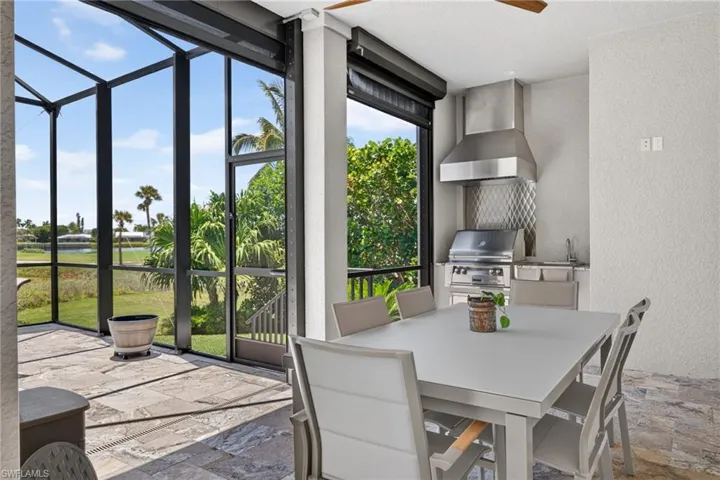 Screened patio featuring an outdoor kitchen with stainless steel appliances, a range hood, and a built-in sink