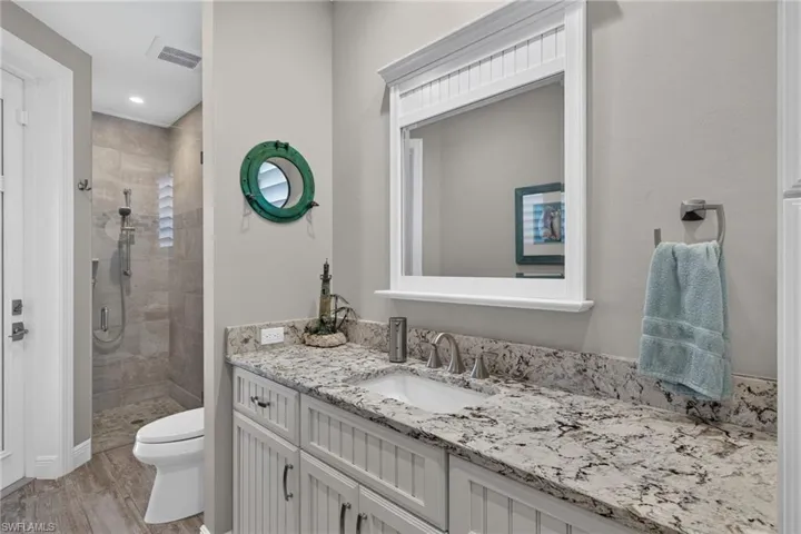 Pool Bath w/ vanity featuring a stone countertop with an undermount sink, brushed nickel faucet, and beadboard cabinetry