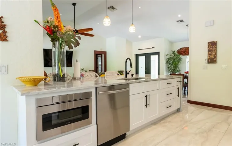 Kitchen featuring stainless steel appliances, a sink, vaulted ceiling, light marble finish flooring, and white cabinets