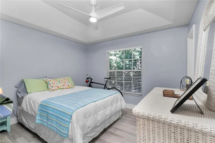 Bedroom with a ceiling fan, wood finished floors, and a tray ceiling