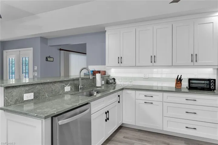 Kitchen with light stone counters, stainless steel dishwasher, white cabinets, and decorative backsplash